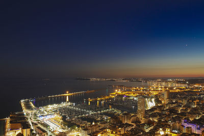 Illuminated cityscape by sea against sky at night