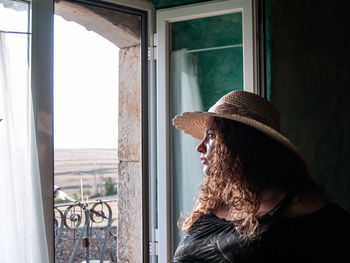 Woman wearing hat while looking through window at home