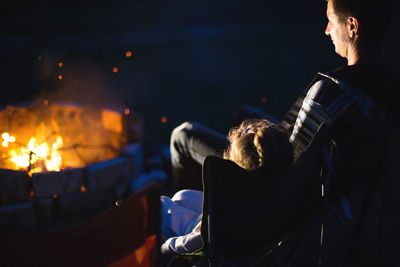 Dad and daughter sit at night by the fire in the open air in the summer in nature. family campin