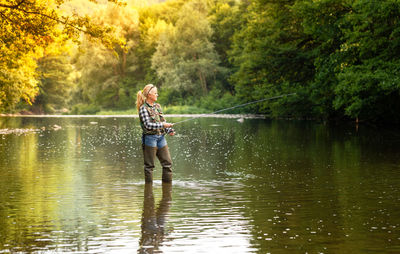 Young attractive woman is fishing with a spinning rod in the river on a clear summer sunny day.