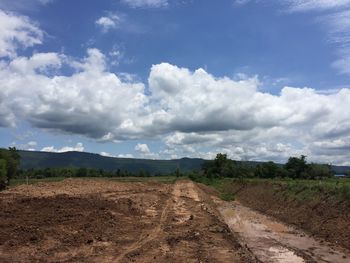 Dirt road amidst field against sky