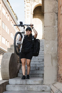 Female delivery person carrying cycle while moving down on steps