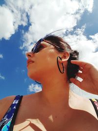 Low angle view of woman wearing sunglasses against cloudy sky