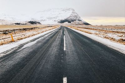 Road on snow covered landscape against sky