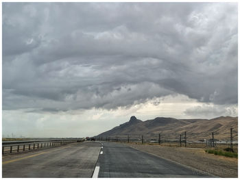 Road passing through landscape against cloudy sky