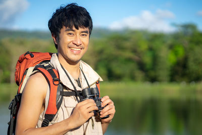 Side view of young man photographing while standing against lake