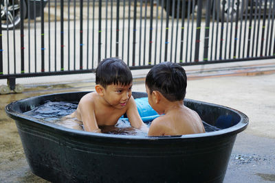 Shirtless brothers sitting in bucket at yard