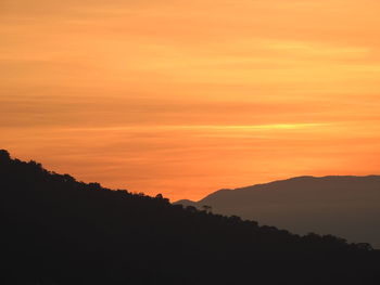 Scenic view of silhouette mountains against orange sky