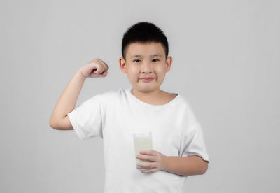 Portrait of smiling boy drinking glass against white background