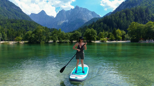Woman paddleboarding on lake against mountains