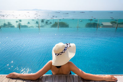 Woman wearing hat while swimming in pool against sea