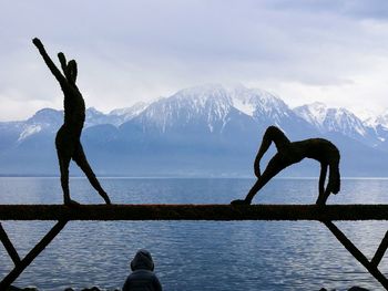 Statues on railing over lake against mountains