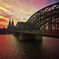 Hohenzollern bridge over river by cologne cathedral against sky during sunset