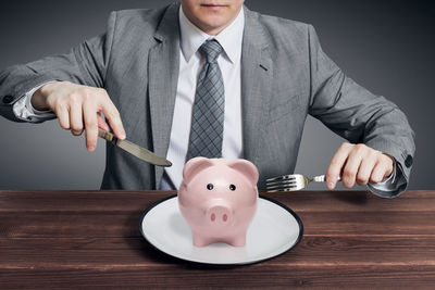 Midsection of businessman holding piggy bank on table
