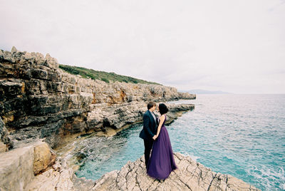 Rear view of woman standing on rock by sea against sky