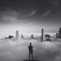 Silhouette man standing by modern city covered with cloudscape against sky