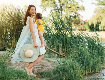 Woman carrying baby while standing against plants
