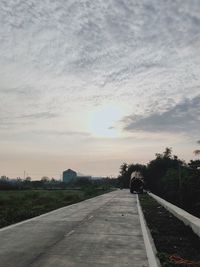 Road by trees against sky during sunset