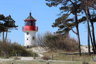 Lighthouse by trees on field against sky