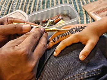Cropped image of parent applying henna tattoo on child hand at home