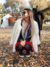 Woman in warm clothing and sunglasses crouching on footpath