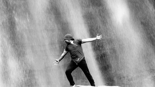 Man with arms outstretched standing against waterfall