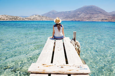 Greece, cyclades islands, amorgos, woman sitting on the edge of a wooden pier, nikouria island