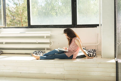 Side view of woman sitting on window