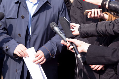 Cropped hands of journalists holding microphones in front of man