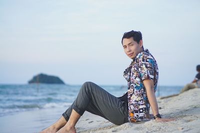 Side view portrait of man sitting at beach against sky