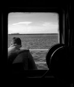 Rear view of man looking at sea through window