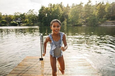 Portrait of excited girl running on jetty after swimming in lake