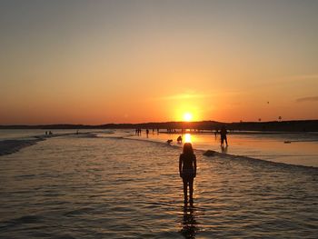 Silhouette people standing on beach against sky during sunset