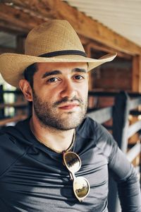 Portrait of man wearing hat while leaning on fence at farm