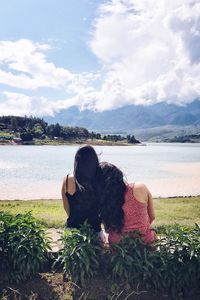 Rear view of female friends sitting at beach against cloudy sky during sunny day