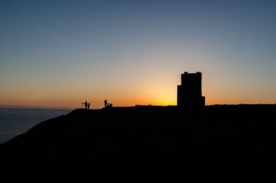 Silhouette man by sea against clear sky during sunset