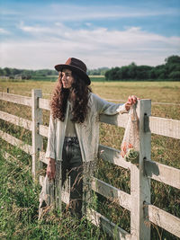 Smiling woman standing by fence on field against sky