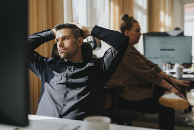 Thoughtful businessman with hands behind head leaning on chair at office
