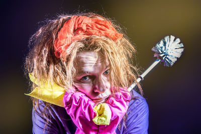 Portrait of woman holding cleaning brush against black background