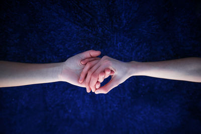 Cropped image of couple holding hands against blue background