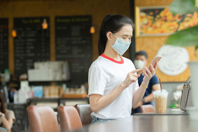 Woman wearing mask using phone at cafe