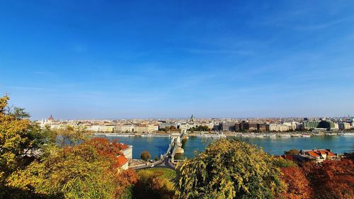 High angle view of city by river against blue sky