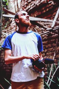 Thoughtful young man photographing while standing against brick wall