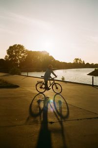 Silhouette woman riding bicycle on road by lake against sky