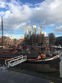 Boats moored at harbor by buildings in city against sky