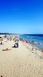 View of people on beach against clear blue sky