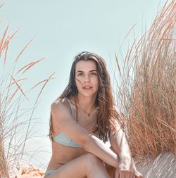 Portrait of young woman sitting on field against sky