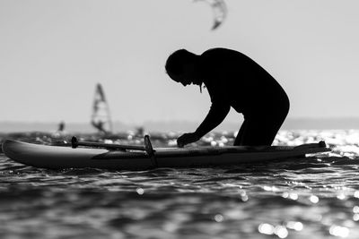 Side view of silhouette man with paddleboard in sea against sky