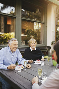 Smiling senior man with female friends having dessert at outdoor restaurant
