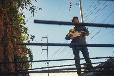 Man on electricity pylon against sky